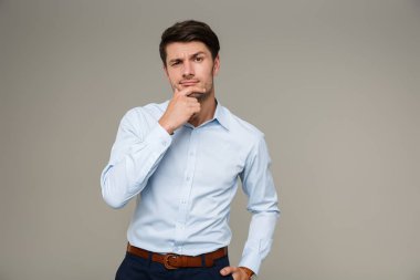 Resmi kıyafetler giyen, kameraya bakıp çenesine dokunan ciddi bir adamın görüntüsü.