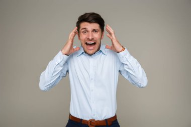 Resmi giysiler giymiş korkmuş genç bir adamın resmi. Kameraya bağırıyor ve el kaldırıyor.