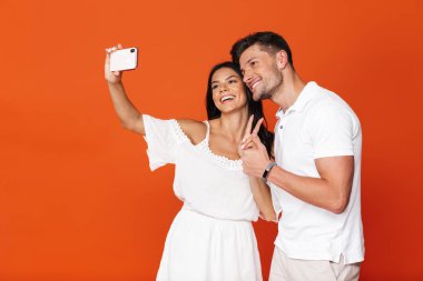 Mutlu, mutlu, mutlu, genç, harika, sevgi dolu çift kırmızı duvarın arkasında izole bir şekilde poz veriyor. Cep telefonlarıyla selfie çekiyorlar..