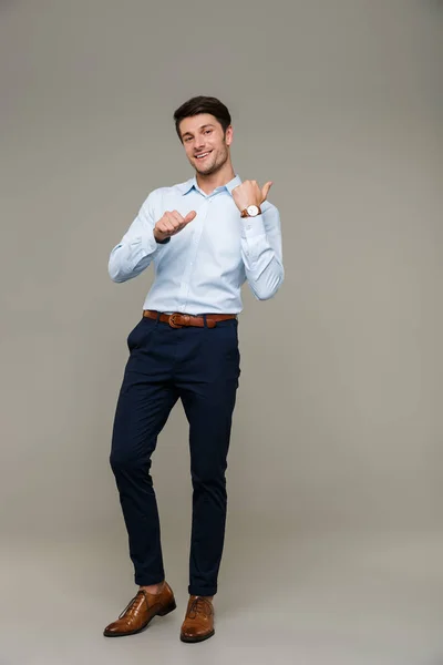 Imagem de homem bonito alegre vestindo roupas formais sorrindo e apontando os dedos para trás no copyspace — Fotografia de Stock