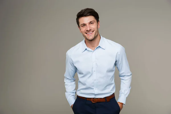 Image of happy brunette man wearing formal clothes smiling at camera with hands in pockets — Stock Photo, Image