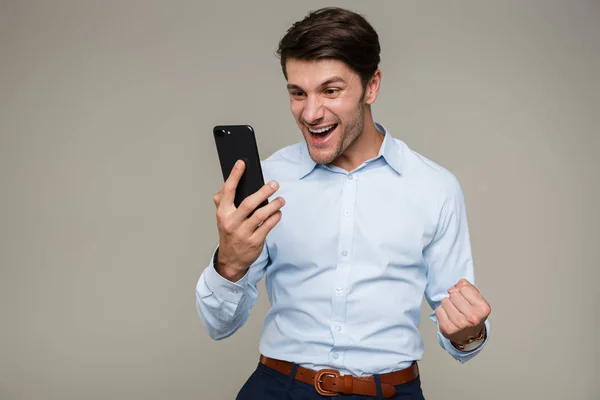 Εικόνα του εκστατικού ευτυχισμένου άνδρα που φοράει επίσημα ρούχα χαμογελώντας και κοιτάζοντας το κινητό του — Φωτογραφία Αρχείου