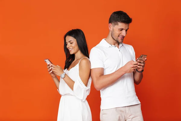 Mladý úžasný milující pár představovat izolované přes červenou zeď pozadí pomocí mobilních telefonů. — Stock fotografie