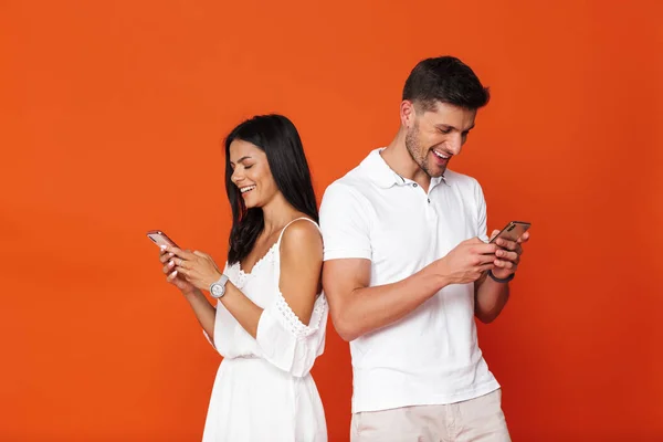Mladý úžasný milující pár představovat izolované přes červenou zeď pozadí pomocí mobilních telefonů. — Stock fotografie