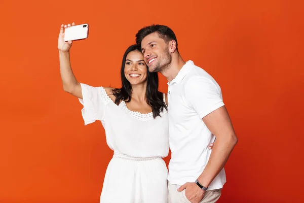 Feliz positivo complacido joven pareja amorosa increíble posando aislado sobre fondo de pared roja tomar selfie por los teléfonos móviles . — Foto de Stock