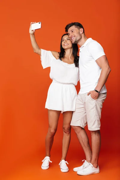 Feliz positivo complacido joven pareja amorosa increíble posando aislado sobre fondo de pared roja tomar selfie por los teléfonos móviles . — Foto de Stock