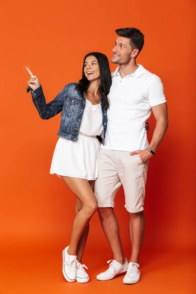 Optimista sonriente atractiva pareja amorosa increíble posando aislado sobre fondo de pared roja señalando . — Foto de Stock