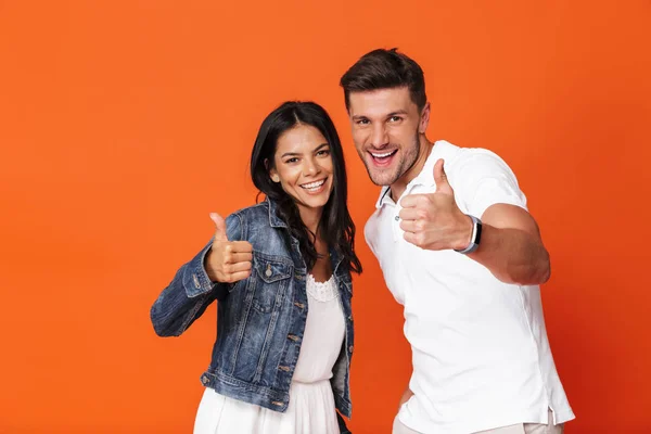 Alegre atractivo increíble pareja amorosa posando aislado sobre fondo de pared roja mostrando pulgares hacia arriba gesto . — Foto de Stock