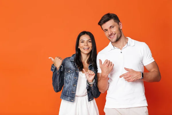 Optimista sonriente atractiva pareja amorosa increíble posando aislado sobre fondo de pared roja señalando . — Foto de Stock