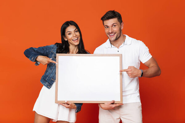 Cheerful positive optimistic attractive loving couple isolated over red wall background holding copyspace blank.