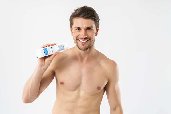 Guapo sonriente dentadura joven hombre desnudo sosteniendo pasta de dientes aislado sobre fondo blanco . —  Fotos de Stock