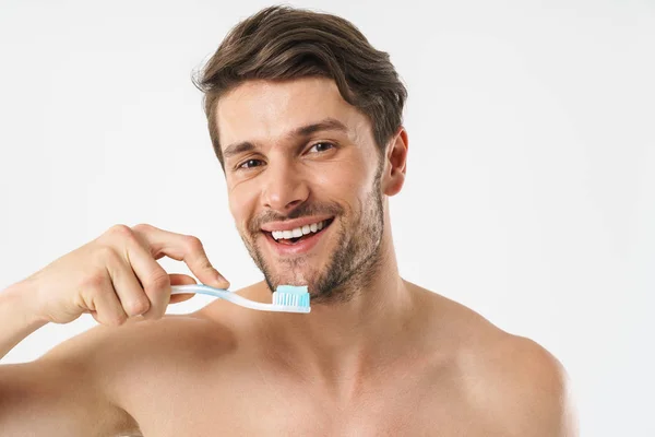 Cheery positive young naked man brushing his teeth isolated over white background. — Stockfoto