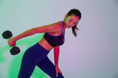 Çekici, genç bir fitness kadını, el fenerleriyle izole edilmiş, kolları için halterlerle egzersiz yapıyor..