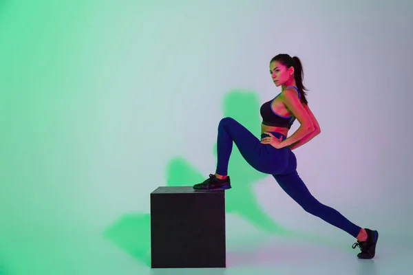 Beautiful young sports woman posing isolated with led flash lights make stretching exercises. — Stock Photo, Image