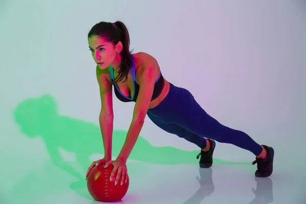Concentrated young fitness woman isolated with led flash lights make exercises with ball. — Stock Photo, Image