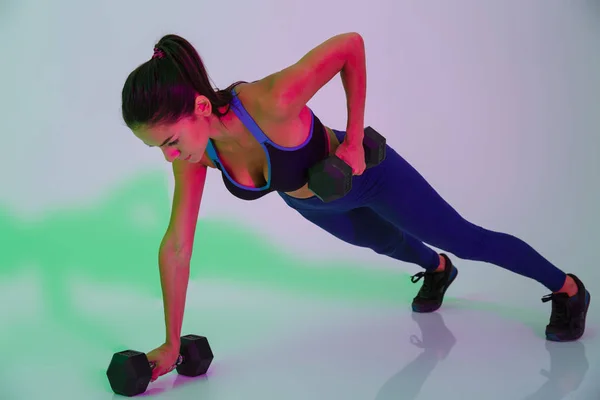 Atractiva joven mujer fitness aislada con luces led flash hacer ejercicios con pesas para los brazos . —  Fotos de Stock