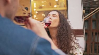 Güzel, genç, kıvırcık saçlı, esmer kadın karavanın yanında otururken erkek arkadaşıyla gülümseyip şarap içiyor.