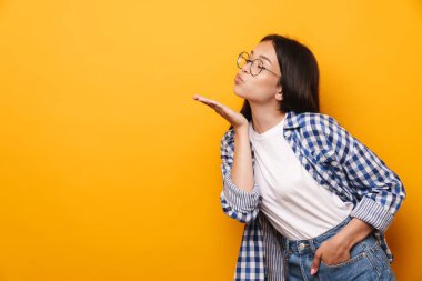İyimser, gözlüklü genç bir kız. Sarı duvar arkasında izole bir şekilde öpüşüyor..