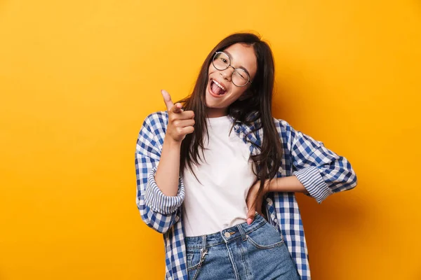 Sonriente emocional joven linda adolescente en gafas posando aislado sobre fondo amarillo de la pared que apunta a usted . —  Fotos de Stock