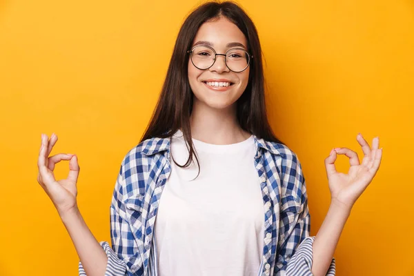 Zadowolony optymistyczne młody słodkie nastolatek dziewczyna w okulary medytować izolowane nad żółtym tle ściany. — Zdjęcie stockowe