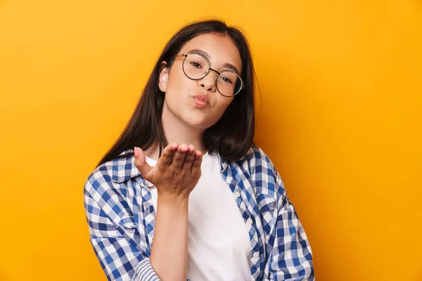 Pozytywny optymistyczne młody słodkie nastolatek dziewczyna w okulary pozowanie izolowane nad żółtą ścianę tło dmuchanie pocałunki. — Zdjęcie stockowe