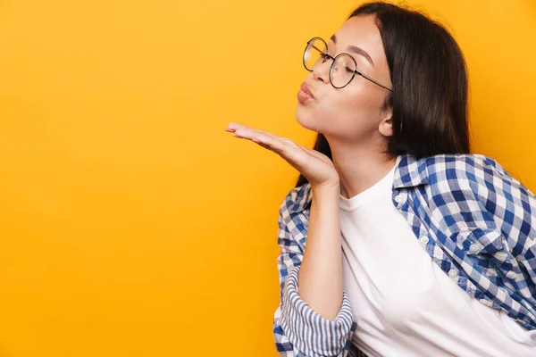 Positivo otimista jovem bonito adolescente em óculos posando isolado sobre amarelo parede fundo soprando beijos . — Fotografia de Stock