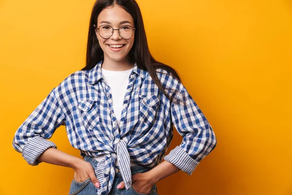 긍정적 이고 행복 한 젊고 귀여운 십 대 소녀가 노란 벽 위에 고립된 채 안경을 쓰고 있다. — 스톡 사진
