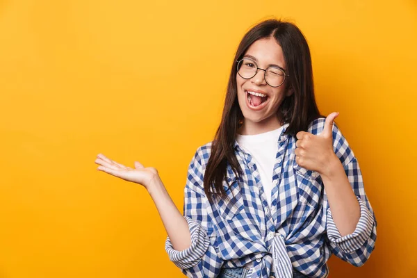 Feliz satisfeito sorrindo jovem bonito adolescente menina em óculos posando isolado sobre amarelo parede fundo mostrando copyspace fazer polegares para cima . — Fotografia de Stock