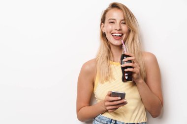 Şaşırtıcı genç güzel bir kadın beyaz duvar arkasında izole bir şekilde poz veriyor cep telefonu kullanıyor soda içiyor..