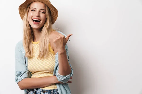 Sorridente felice sorprendente giovane bella donna che indossa cappello posa isolata su sfondo bianco muro che punta al copyspace . — Foto Stock