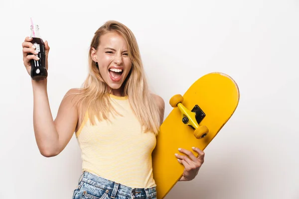 Χαρούμενη καταπληκτική νεαρή όμορφη γυναίκα θέτουν απομονωμένη πάνω από λευκό φόντο τοίχο κρατώντας skateboard πόσιμο σόδα. — Φωτογραφία Αρχείου