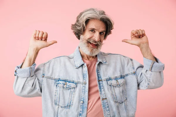 Portrait of cheerful old man with gray beard pointing fingers backward at copyspace i