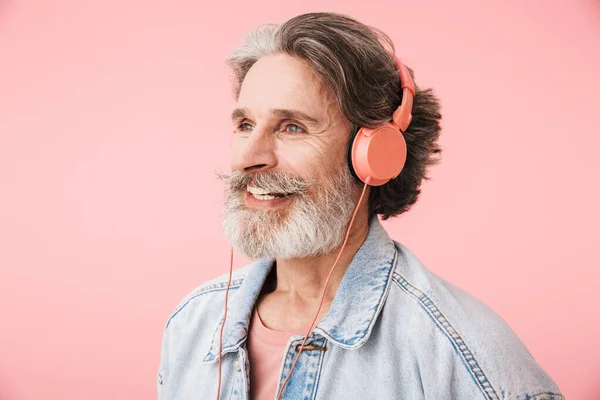 Portrait closeup of joyful old man 70s with gray beard singing while listening to music with headphones
