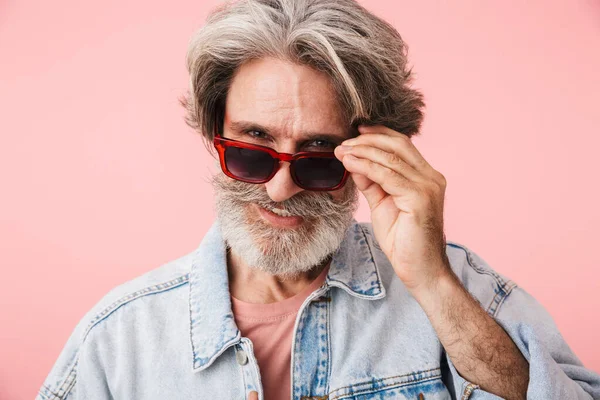 Portret close-up van vrolijke oude man jaren 70 met grijze baard kijken naar de camera en het aanraken van zijn zonnebril — Stockfoto