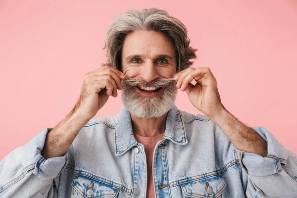 Porträt eines fröhlichen alten Mannes mit grauem Bart, der in die Kamera lächelt und seinen Schnurrbart berührt — Stockfoto