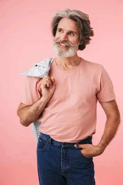 Portret przystojnego dojrzałego mężczyzny lat 70-tych z szarą brodą uśmiechającego się i trzymającego jeansową kurtkę na ramieniu — Zdjęcie stockowe