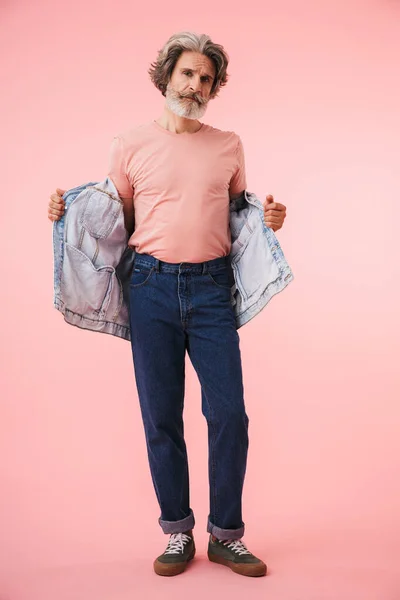 Full length portrait of stylish mature man 70s with gray beard looking at camera and holding his denim jacket — Stock Photo, Image