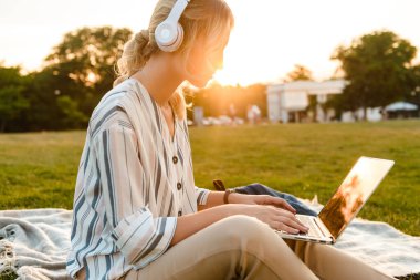 Güzel sarışın kız parkta çimenlikte dinleniyor.