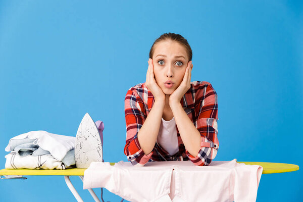 Portrait of surprised housewife wearing casual plaid shirt ironi