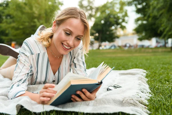 Piękna młoda blondynka relaksująca się na trawniku w parku — Zdjęcie stockowe