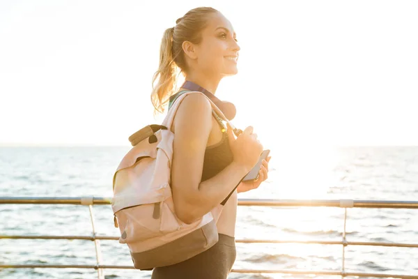 Vacker ung fitness kvinna som bär ryggsäck promenader vid piren — Stockfoto