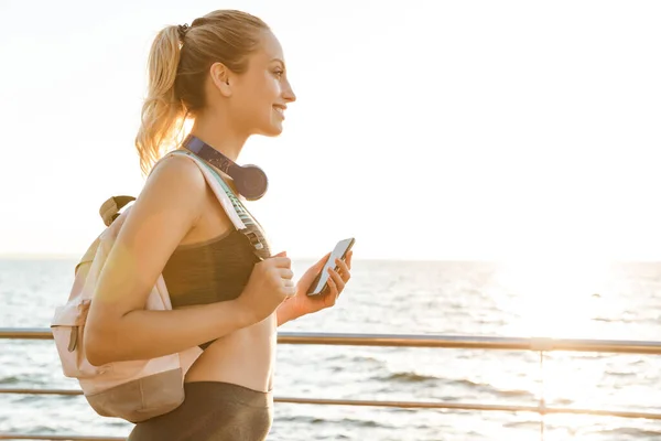 Hermosa joven fitness mujer llevando mochila caminando en el muelle — Foto de Stock