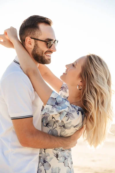 Foto von attraktiven romantischen Paar lachen und umarmen beim Spazierengehen am sonnigen Strand — Stockfoto