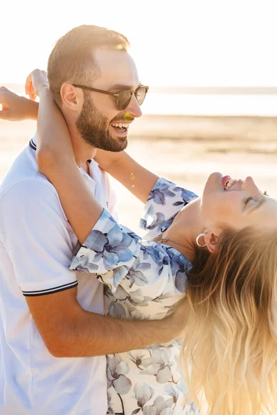 Foto von lustigen glücklichen Paar lachen und umarmen beim Spazierengehen am sonnigen Strand — Stockfoto