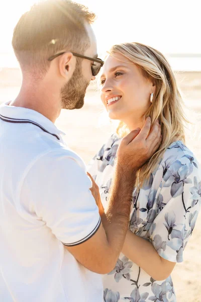 Фото кавказької щасливої пари, яка посміхається і обіймається під час прогулянки на сонячному пляжі — стокове фото