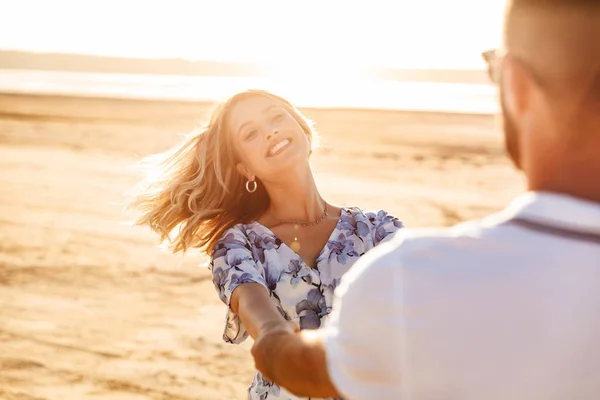 Foto von schönen freudigen Paar einander lächelnd und wirbelnd beim Spazierengehen am sonnigen Strand — Stockfoto