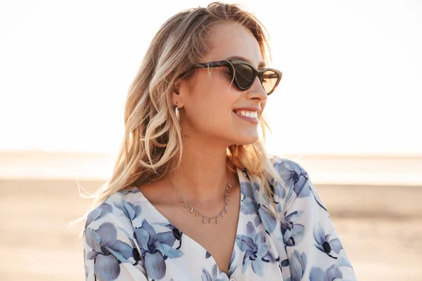 Foto de una joven encantadora sonriendo y mirando a un lado mientras camina en la playa soleada —  Fotos de Stock