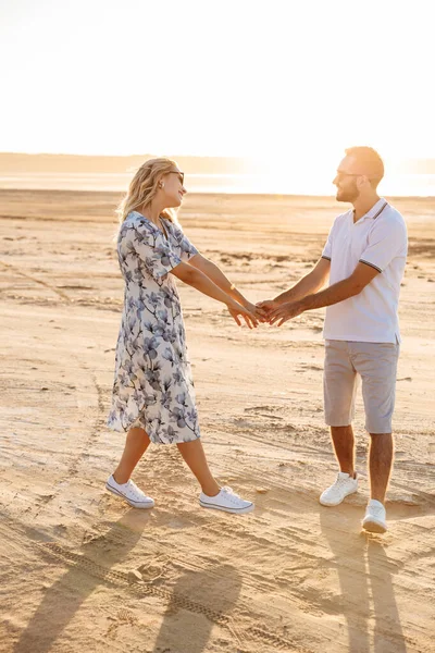 Güneşli sahilde yürürken gülümseyen ve dans eden komik bir çiftin fotoğrafı.