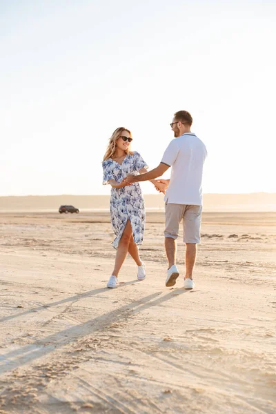 Güneşli sahilde yürürken gülümseyen ve dans eden hoş bir çiftin fotoğrafı.