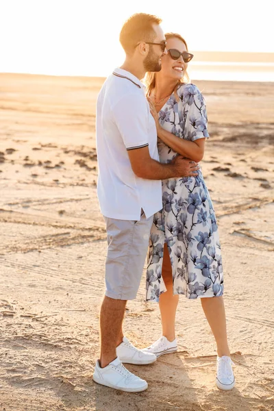 Güneşli sahilde yürürken gülümseyen ve sarılan genç çiftin fotoğrafı. — Stok fotoğraf
